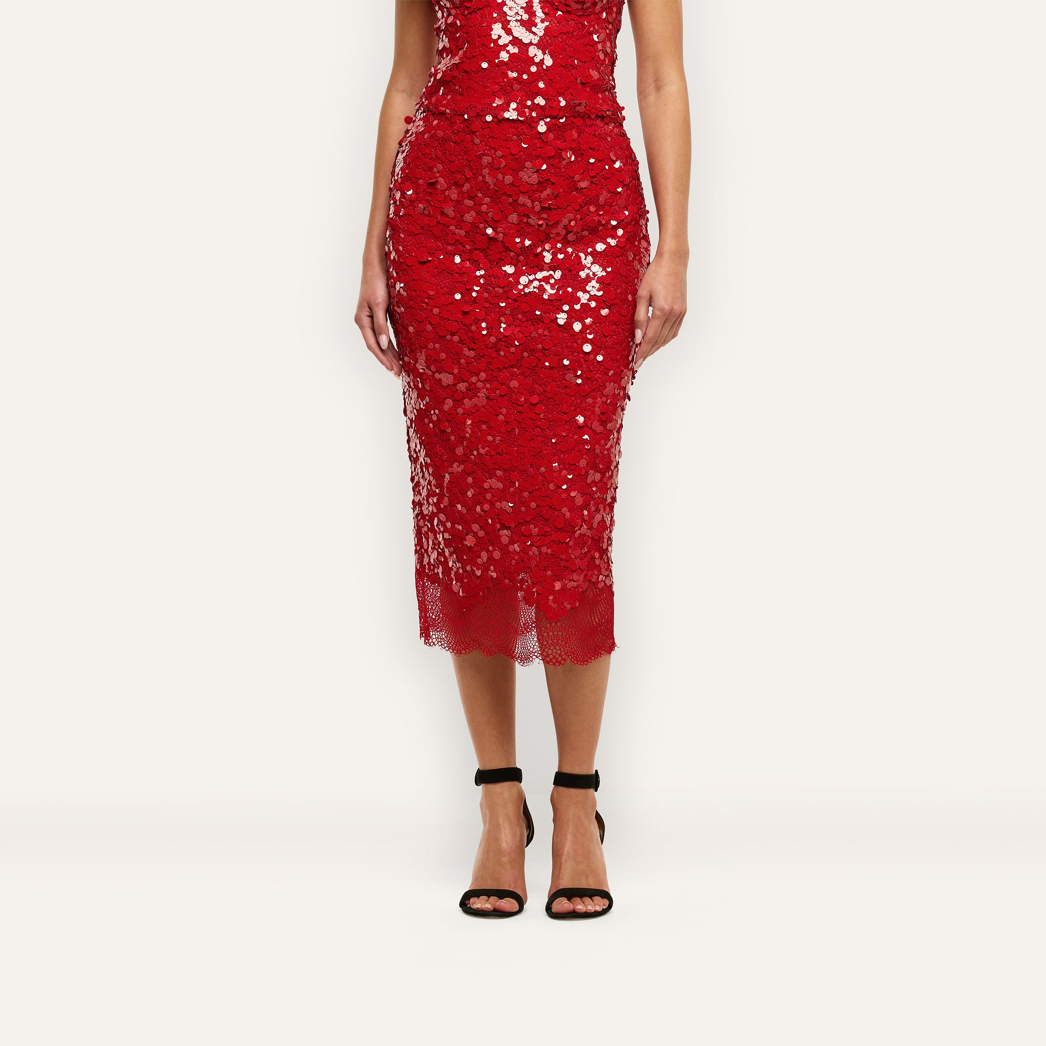 Makena Sequin Pencil Skirt in red with a scalloped lace hem, paired with black ankle-strap heels for a festive look.