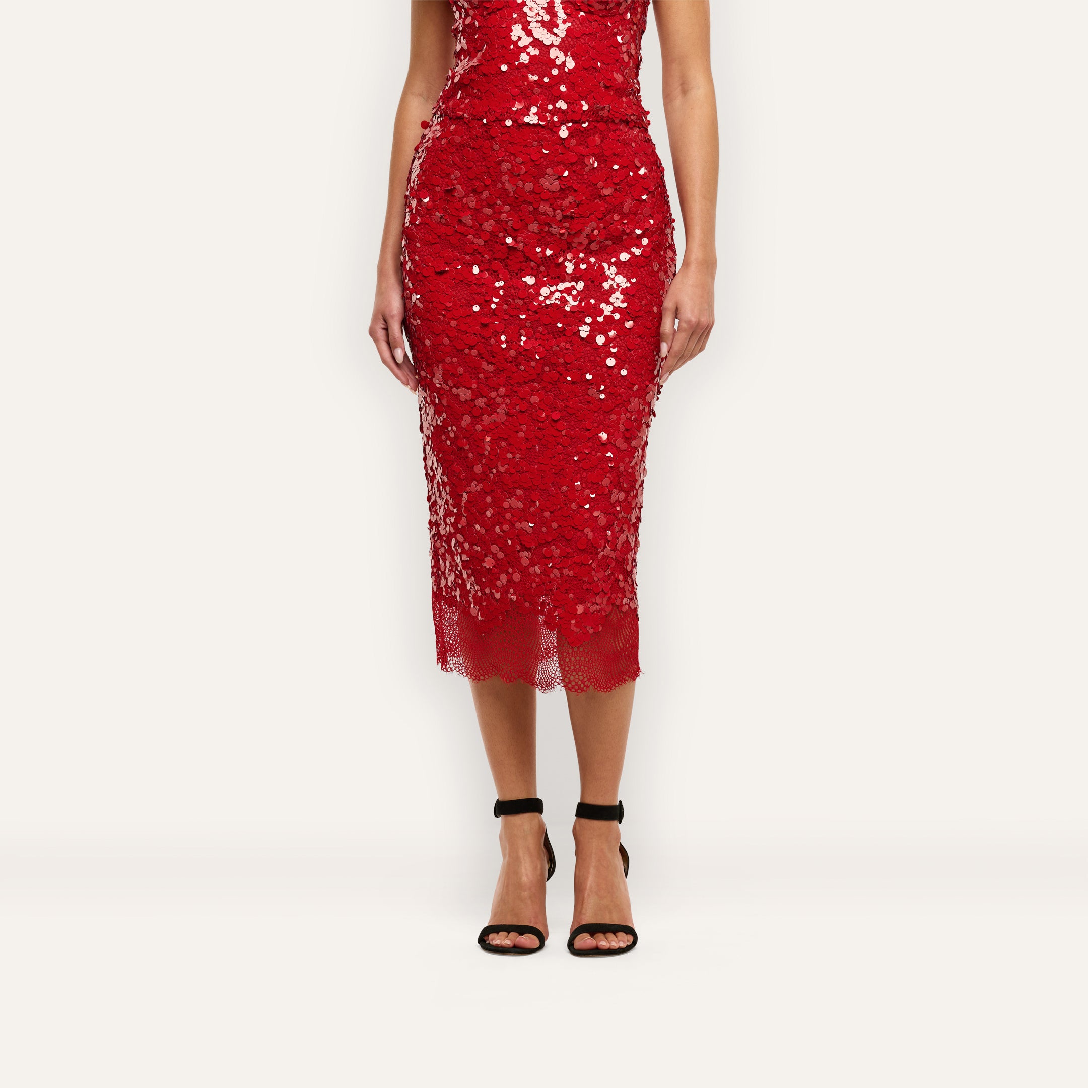 Makena Sequin Pencil Skirt in red with a scalloped lace hem, paired with black ankle-strap heels for a festive look.