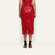 Back view of a person wearing a festive red sequined Makena Sequin Pencil Skirt with a lace hem and black high-heeled sandals.