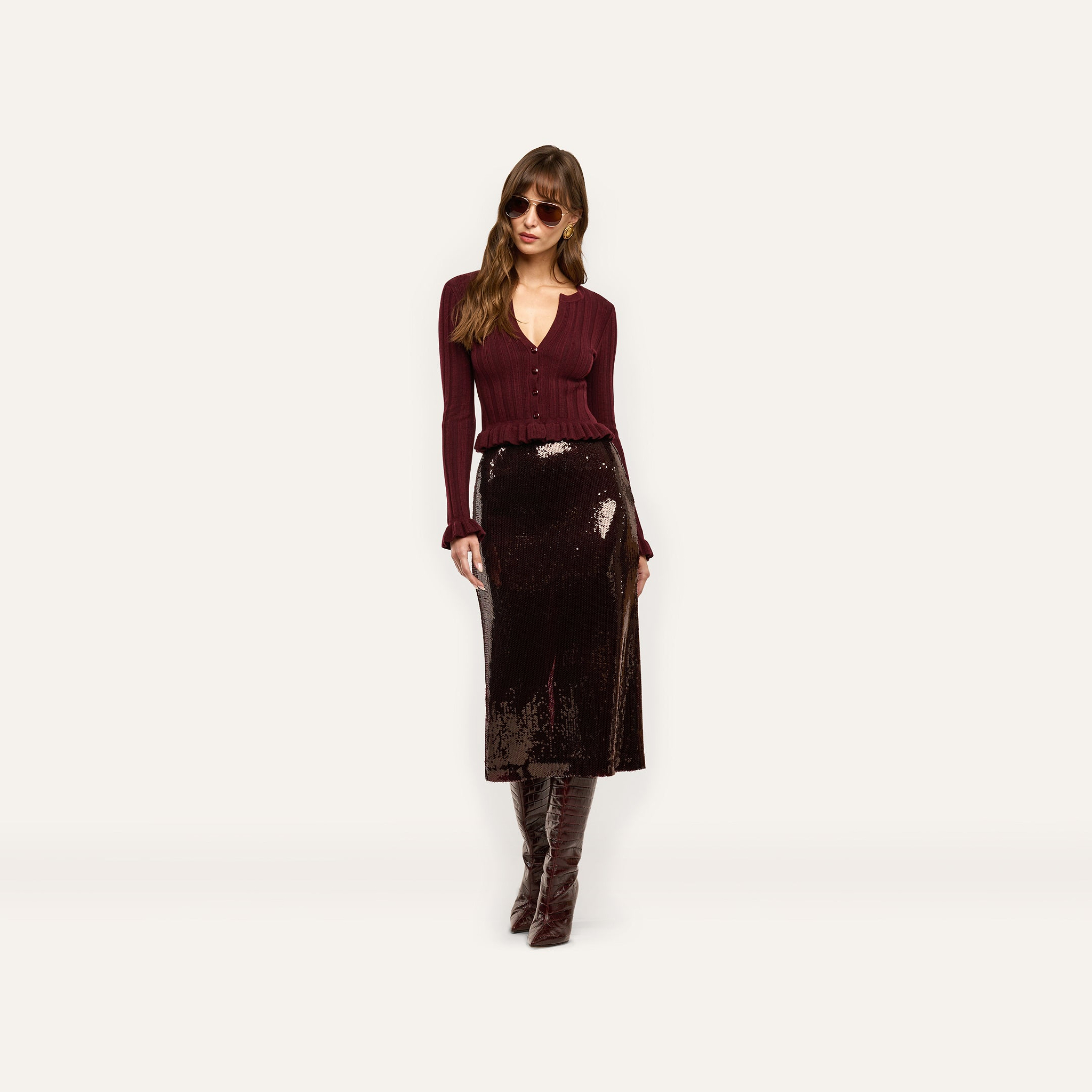 A person wearing a Makena Sequin Pencil Skirt in espresso brown, styled with a burgundy long-sleeved top and knee-high boots.