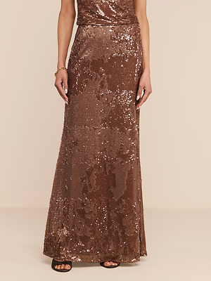 A person in a floor-length, brown Zeta Sequin Maxi Skirt and black open-toe heels stands against a neutral background, with only the lower half of the body visible.