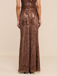 A person stands facing away, wearing a floor-length, sleeveless brown outfit featuring the Zeta Sequin Maxi Skirt by L’AGENCE. The background is plain white, and only the back view of the ensemble is visible.