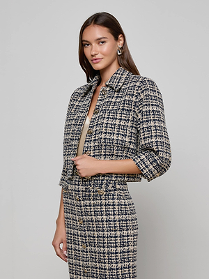 A woman smiles softly as she poses against a light gray background, wearing the L'AGENCE Jia Tweed Jacket with a matching skirt and resting one hand at her waist.