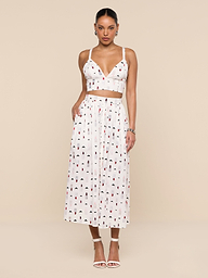 A woman stands against a white background wearing a white crop top and the Seina Poplin Midi Skirt—a high-waisted, ankle-length skirt featuring a small colorful print—paired with white high-heeled sandals.
