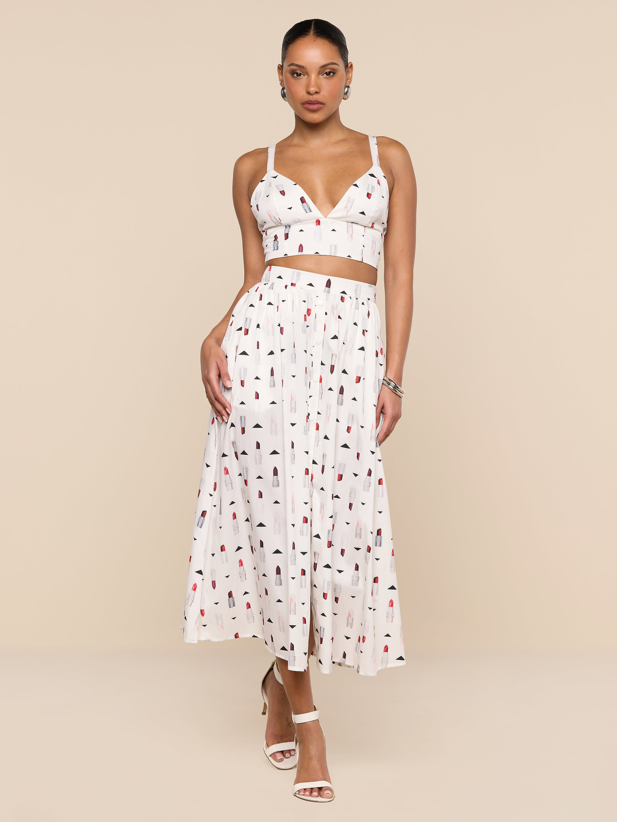 A woman wearing a white sleeveless crop top and the Seina Poplin Midi Skirt—a high-waisted, ankle-length skirt featuring a multicolored abstract print—stands against a plain white background.