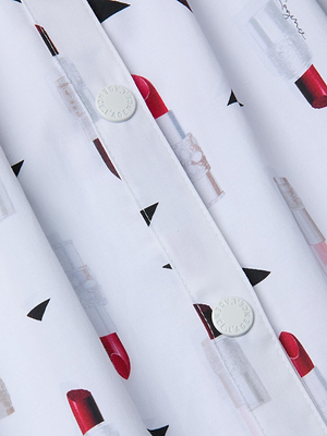 Close-up of a white shirt with playful lipstick print and black triangles, featuring white round buttons—perfect for pairing with the Seina Poplin Midi Skirt for a chic look.