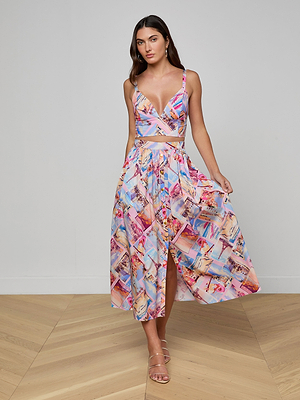 A woman stands indoors on wooden flooring against a plain light gray wall, wearing a colorful postcard print crop top and the Seina Poplin Midi Skirt. She is holding one side of her high-waisted, mid-length skirt.