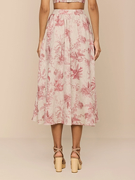 A woman stands with her back to the camera wearing the Seina Linen Midi Skirt, featuring a high waist and pink and white jungle toile print, paired with nude strappy block-heeled sandals.