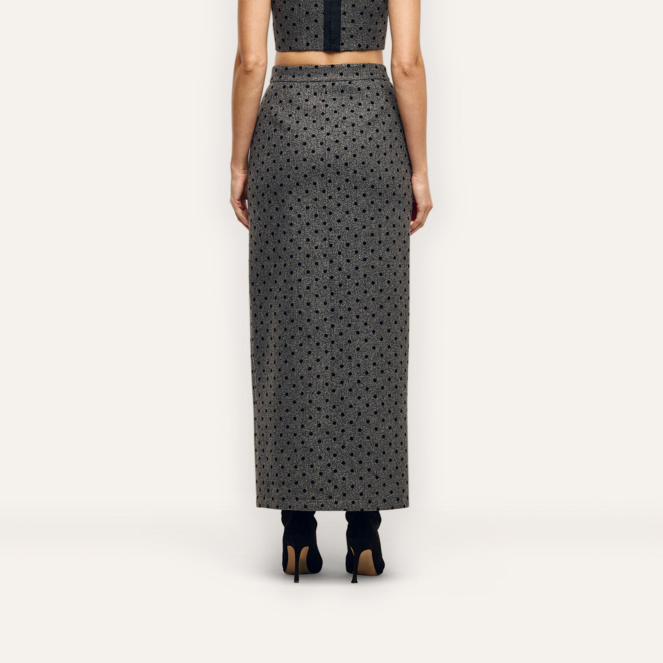 A person viewed from behind, wearing a grey polka-dot Maceline Maxi Skirt and black heeled boots.