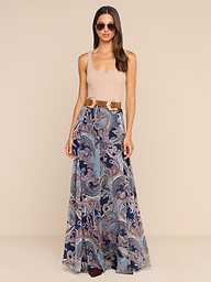 A woman wearing sunglasses, a beige sleeveless top, and the Patrica Maxi Skirt in midnight blue featuring a flowing paisley print with a wide belt, stands against a plain white background.