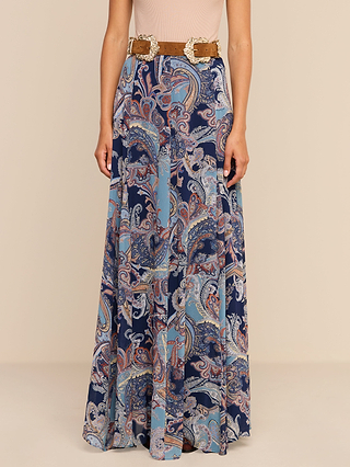 A woman wearing a sleeveless beige top and the Patrica Maxi Skirt, a long, flowing skirt with a midnight blue and multicolor paisley print, accessorized with a wide brown belt featuring decorative buckles.