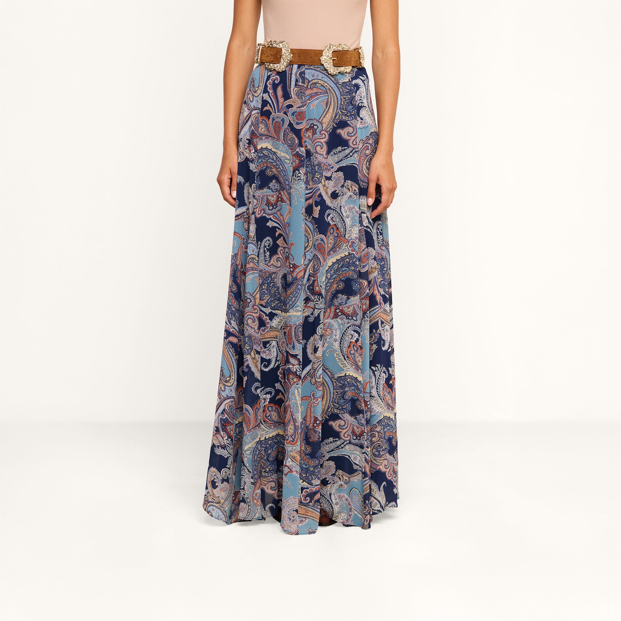 A person wearing the Patrica Maxi Skirt, a high-waisted midnight blue paisley print maxi skirt, paired with a wide brown belt, stands against a plain white background.