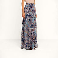 A woman wearing a sleeveless beige top paired with the Patrica Maxi Skirt—a high-waisted, floor-length skirt showcasing an intricate midnight blue and pink paisley print—stands against a plain white background.