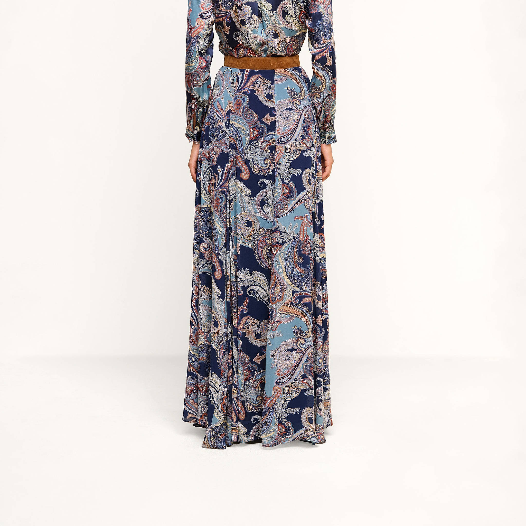 A person is shown from the back, standing against a plain white background, wearing the Patrica Maxi Skirt in midnight blue paisley print with a brown belt.