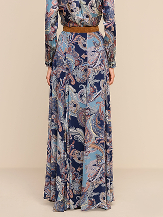 Wearing the Patrica Maxi Skirt, featuring a midnight blue and brown paisley print and paired with a matching top, the person stands with their back to the camera against a plain beige background.