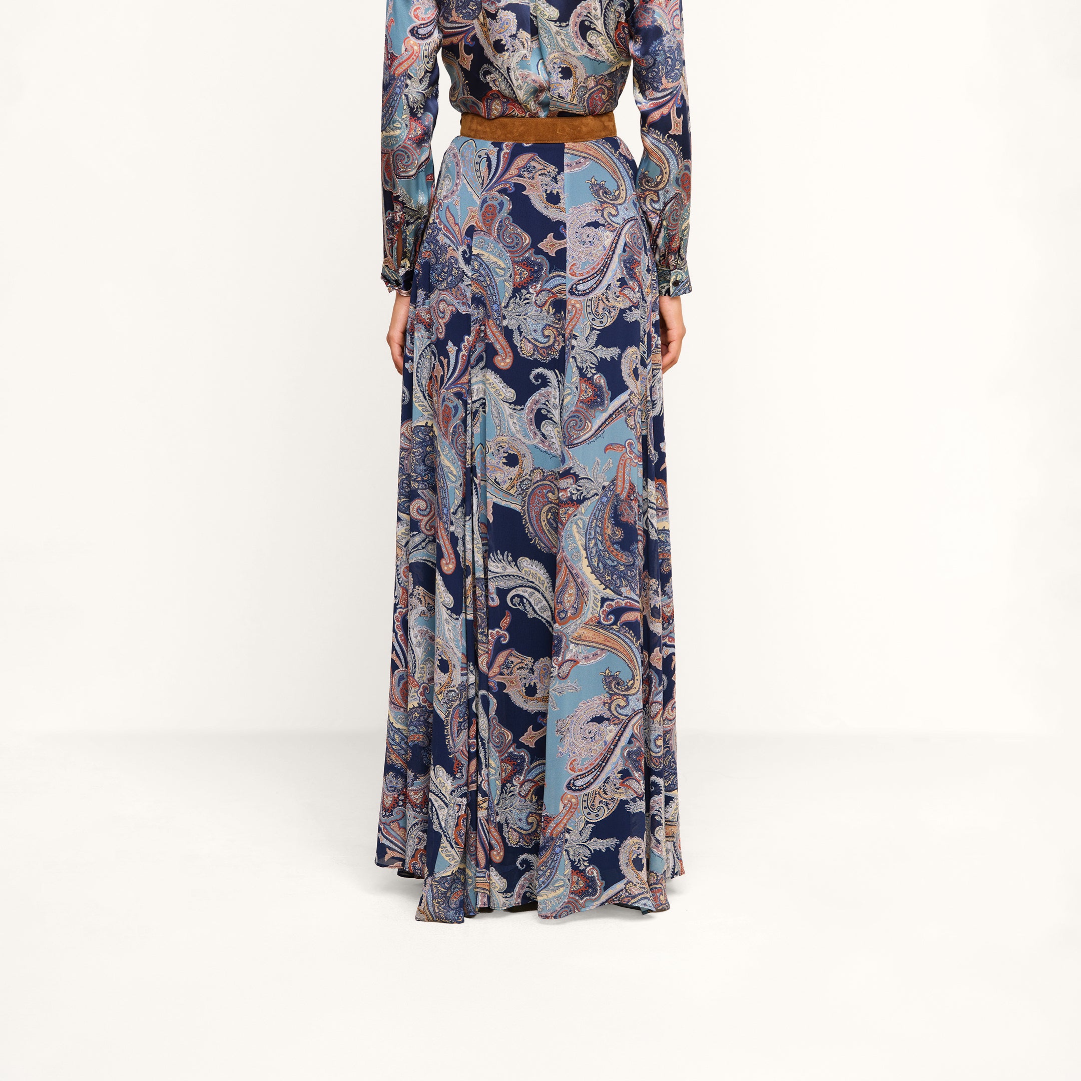 A person is shown from the back, standing against a plain white background, wearing the Patrica Maxi Skirt in midnight blue paisley print with a brown belt.
