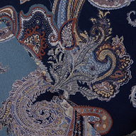 Close-up of overlapping fabric swatches from the Patrica Maxi Skirt, showcasing an intricate paisley print in blue, midnight blue, tan, and orange tones. The detailed designs feature swirling shapes and floral motifs.