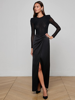 A woman in the Emmarie Maxi Wrap Skirt by L'AGENCE, crafted in black stretch satin with a stylish wrap front.