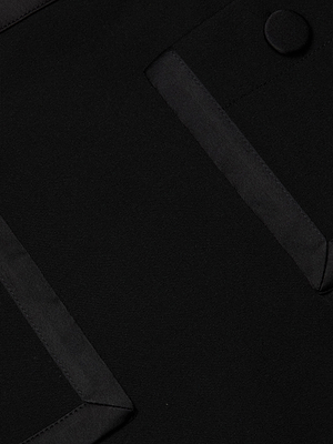 Close-up of black stretch fabric on the Cassiopeia Mini Skirt, featuring two diagonal flap pockets and a round button, all edged with slightly shinier satin trim for a tailored finish.