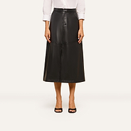 A person wears a white long-sleeve shirt tucked into the high-waisted Robyn Vegan Leather Skirt in black, featuring front seams, paired with black open-toe heels, and stands against a plain background.
