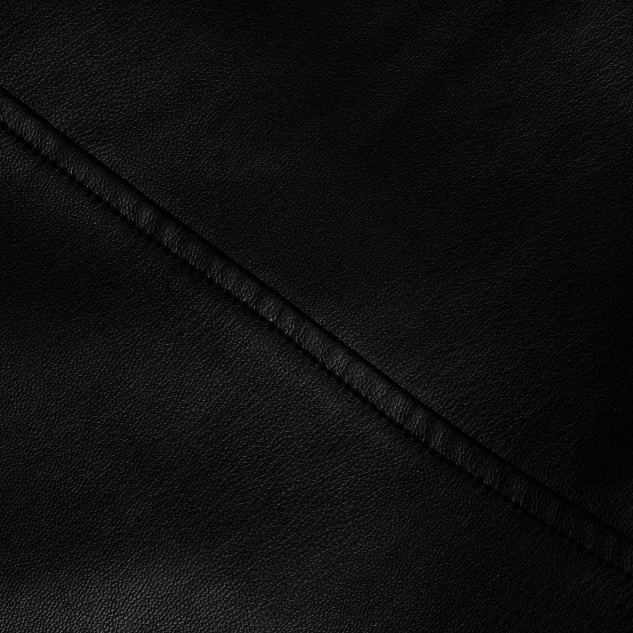 Close-up of the Robyn Vegan Leather Skirt in black, showcasing its smooth, slightly pebbled texture. A diagonal seam runs across the surface, emphasizing the material’s grain and the neat stitching along the seam.