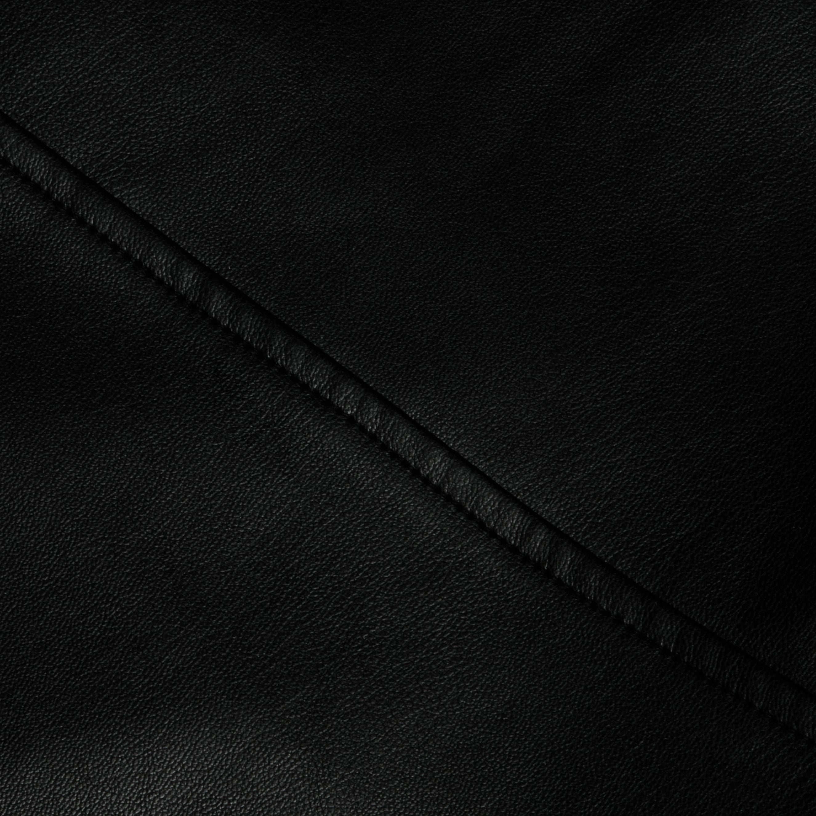Close-up of the Robyn Vegan Leather Skirt in black, showcasing its smooth, slightly pebbled texture. A diagonal seam runs across the surface, emphasizing the material’s grain and the neat stitching along the seam.