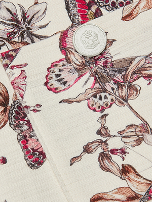 Close-up of the Cyra Low-Rise Mini Skirt: features butterfly print in pink, brown, and black on a cream background with a gold embossed emblem button—ideal for a chic, stylish look.