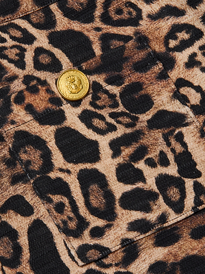 Close-up of the L'AGENCE Cyra Low-Rise Mini Skirt in brown and black leopard print, featuring a gold crest-embossed button on the pocket.