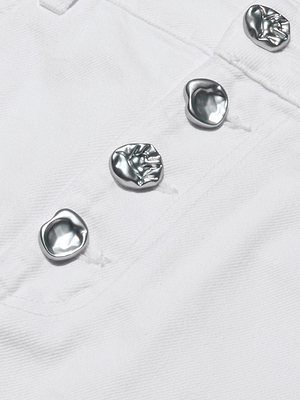 Close-up of the Solene Jean Mini Skirt in white denim with shiny novelty buttons. Each button has an irregular organic shape and textured surface, arranged neatly down the front.