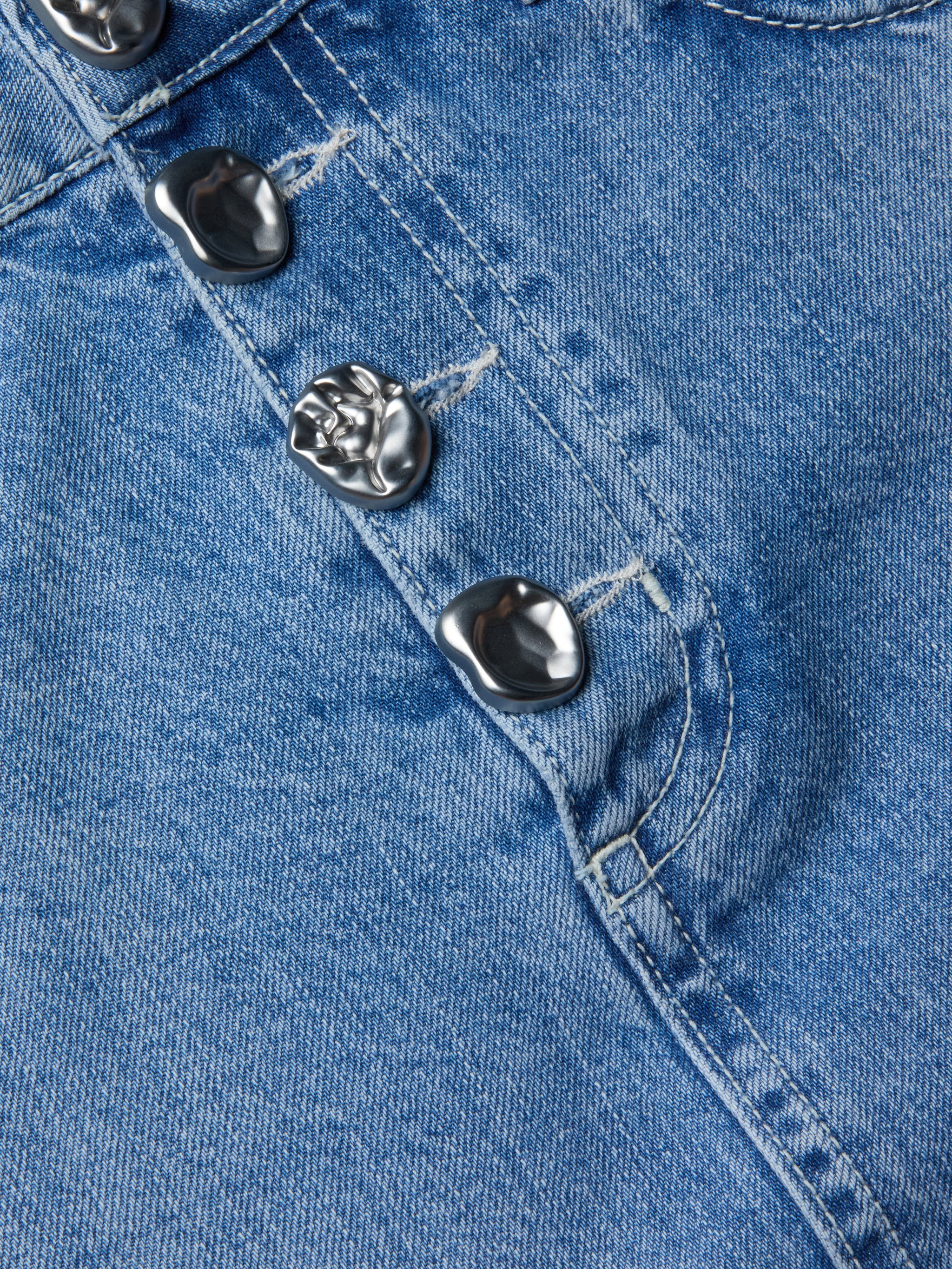 Primo piano della minigonna Solene Jean in denim blu interamente in cotone, con quattro bottoni metallici, cuciture a vista e cucitura della tasca sul lato destro.