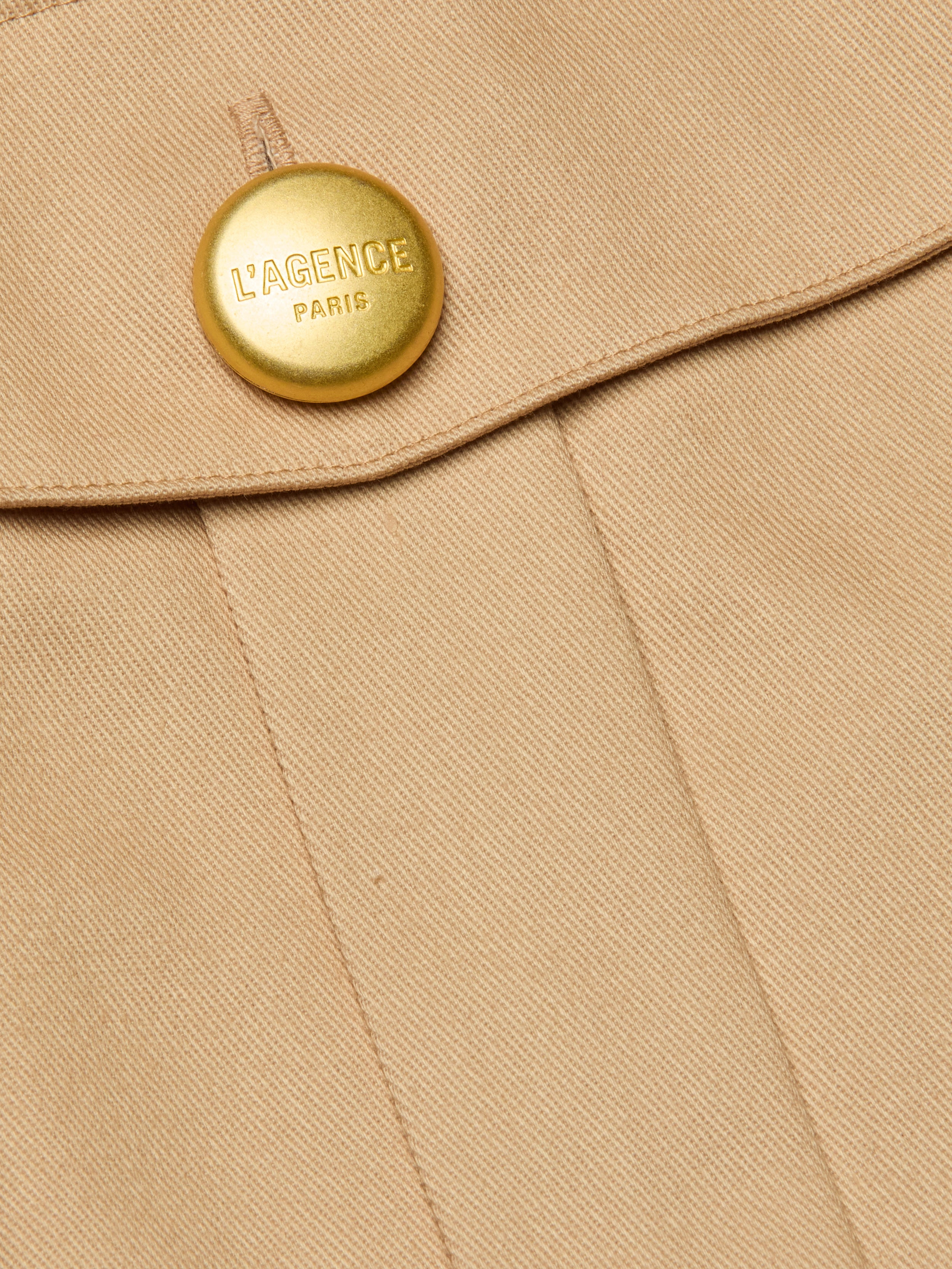 Close-up of the Maelis Mini Skirt in beige, featuring a gold button engraved with LAGENCE PARIS near the seam and flap, highlighting the tailored detail of this high-rise waist design.