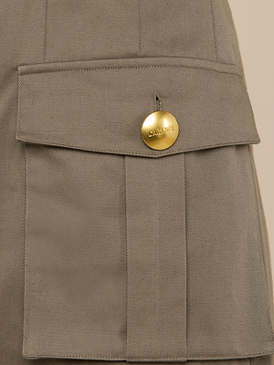 Close-up of the Maelis Mini Skirts khaki cotton twill pocket, featuring a flap secured with a shiny gold LAURENCE-engraved button. The visible stitching and texture add classic cargo pocket detail to the design.