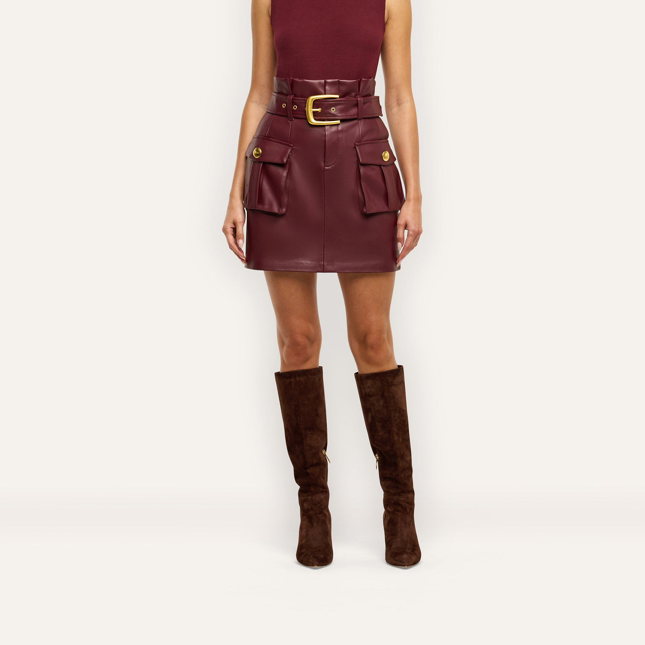 Maelis Vegan Leather Skirt in burgundy, featuring a paperbag mini silhouette, buckled waist belt, two front cargo pockets, and gold hardware.