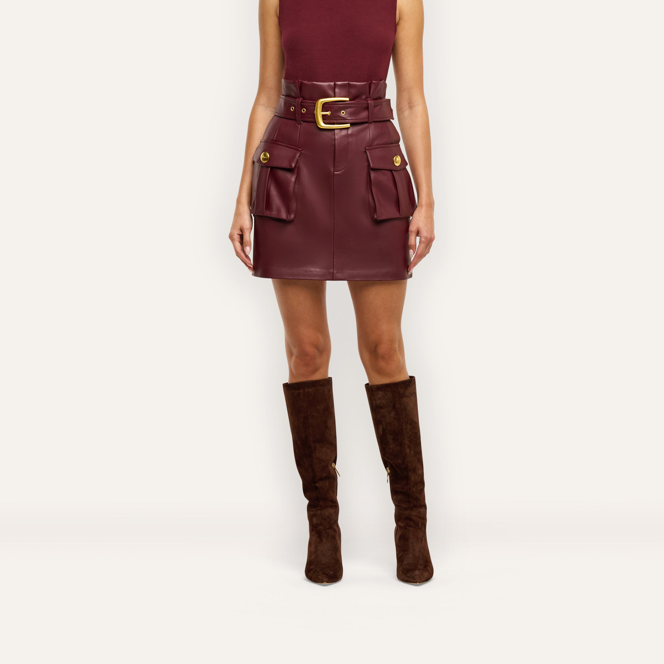 Maelis Vegan Leather Skirt in burgundy, featuring a paperbag mini silhouette, buckled waist belt, two front cargo pockets, and gold hardware.