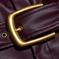 Close-up of a gold-tone belt buckle with the brand name engraved on the frame of a deep burgundy Maelis Vegan Leather Skirt.