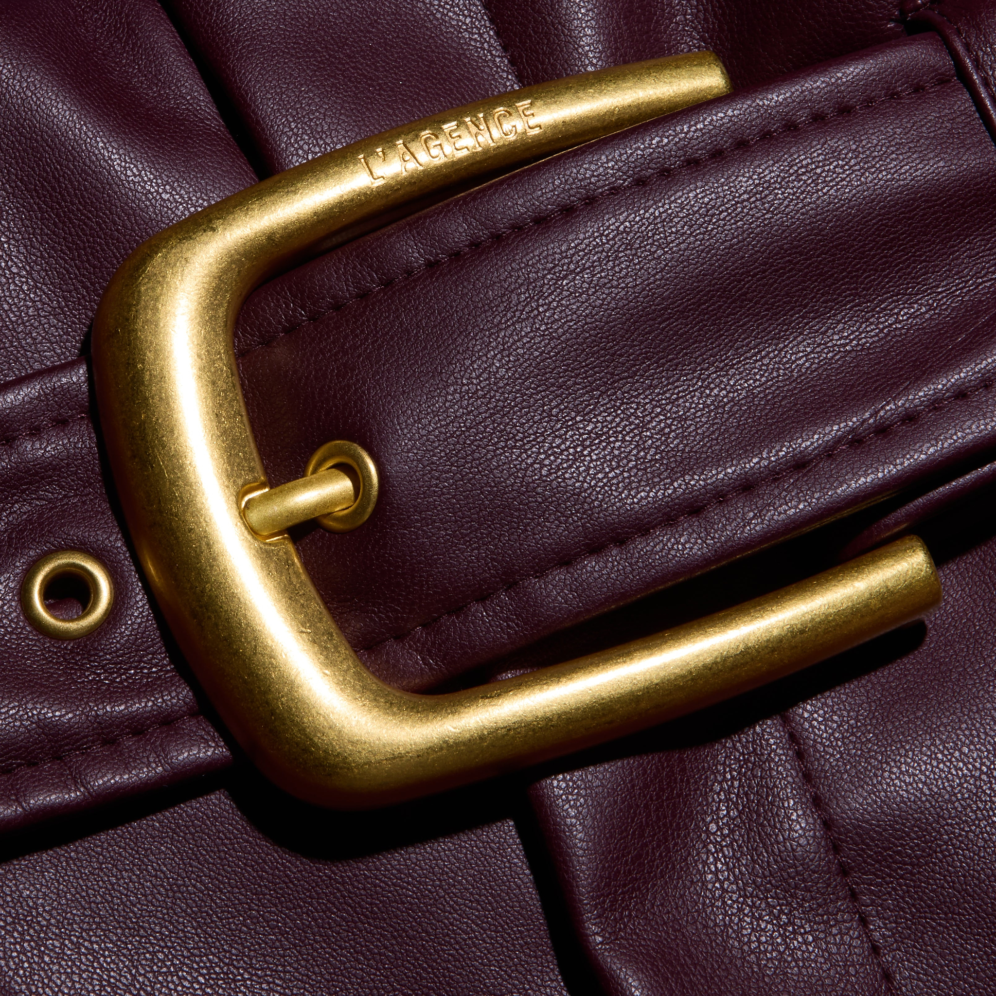 Close-up of a gold-tone belt buckle with the brand name engraved on the frame of a deep burgundy Maelis Vegan Leather Skirt.