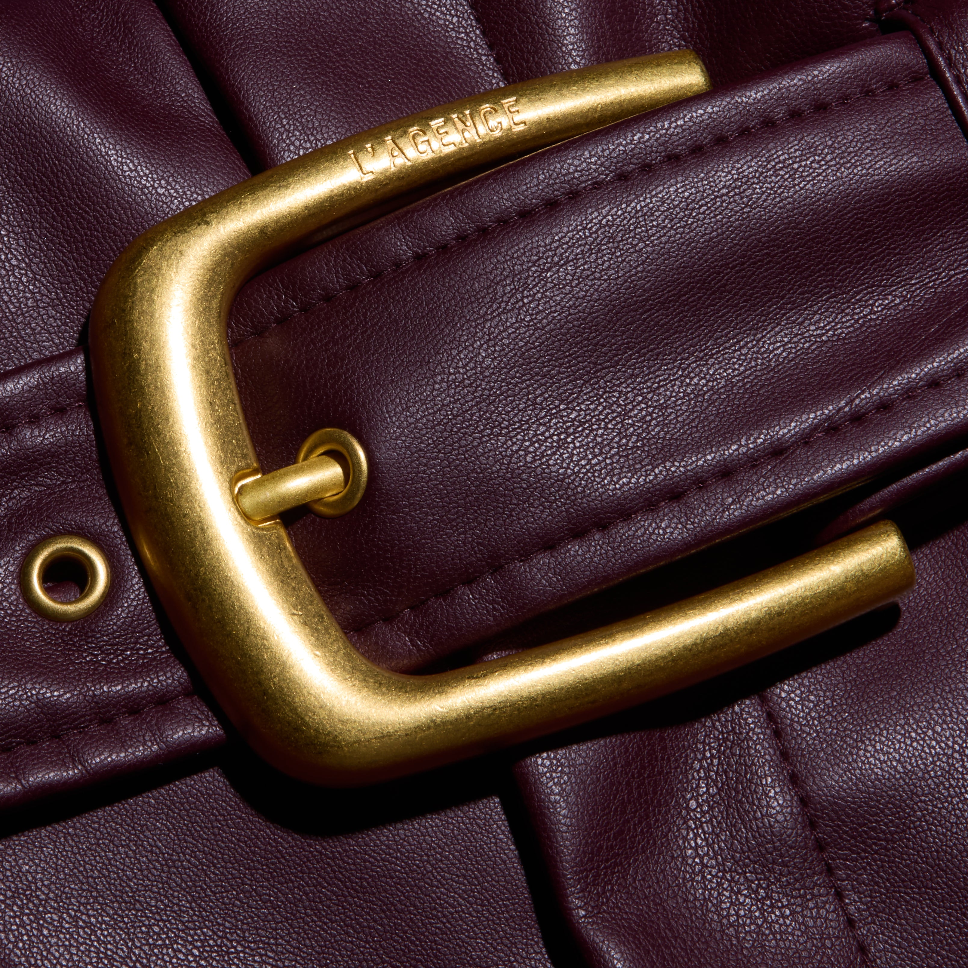 Close-up of a gold-tone belt buckle with the brand name engraved on the frame of a deep burgundy Maelis Vegan Leather Skirt.