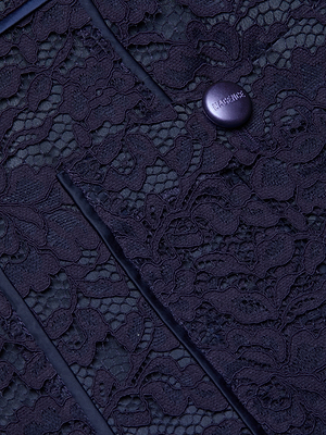 Close-up of Riven Lace Mini Skirt in midnight blue, showcasing its floral lace pattern and a gold BALMAIN-engraved button with a decorative rim. The image highlights the skirts intricate texture and luxurious detail.