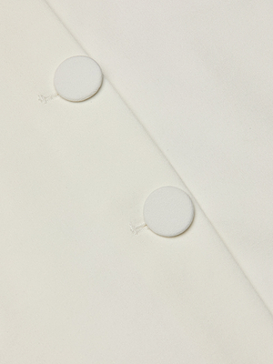 Close-up of the Beah Mini Skirt in white stretch suiting fabric, featuring two round, fabric-covered buttons sewn diagonally. The smooth, neatly tailored material is perfect for a tuxedo-inspired look.