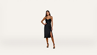 A woman stands against a plain white background wearing a black, sleeveless, knee-length dress with thin straps and a side slit, paired with black high-heeled sandals.