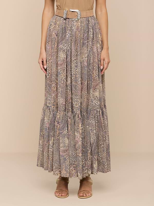 A person wearing a beige top, the Ursie Maxi Skirt—a bohemian paisley leopard print maxi skirt with a belt—and tan sandals stands against a plain light background.