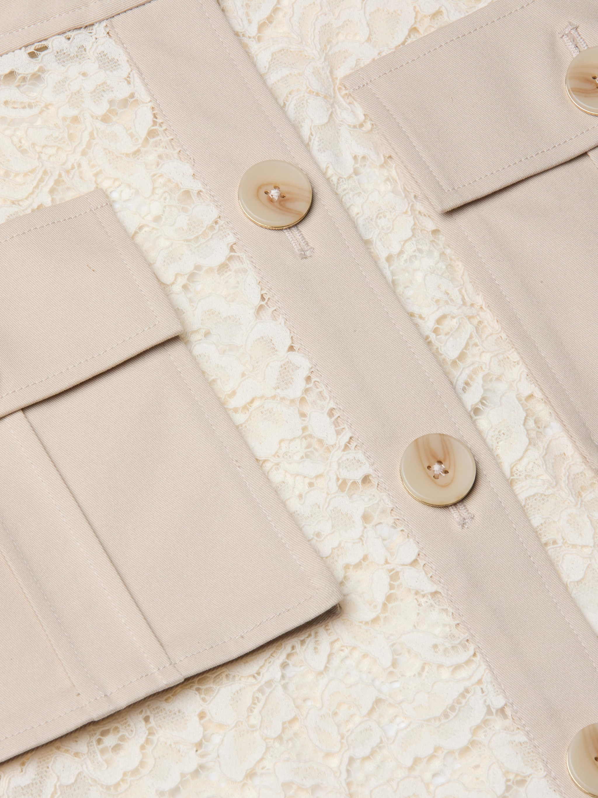 Close-up of the Shae Skirt featuring cream-colored floral lace fabric, beige panels, cargo pockets, and large beige buttons stitched vertically.