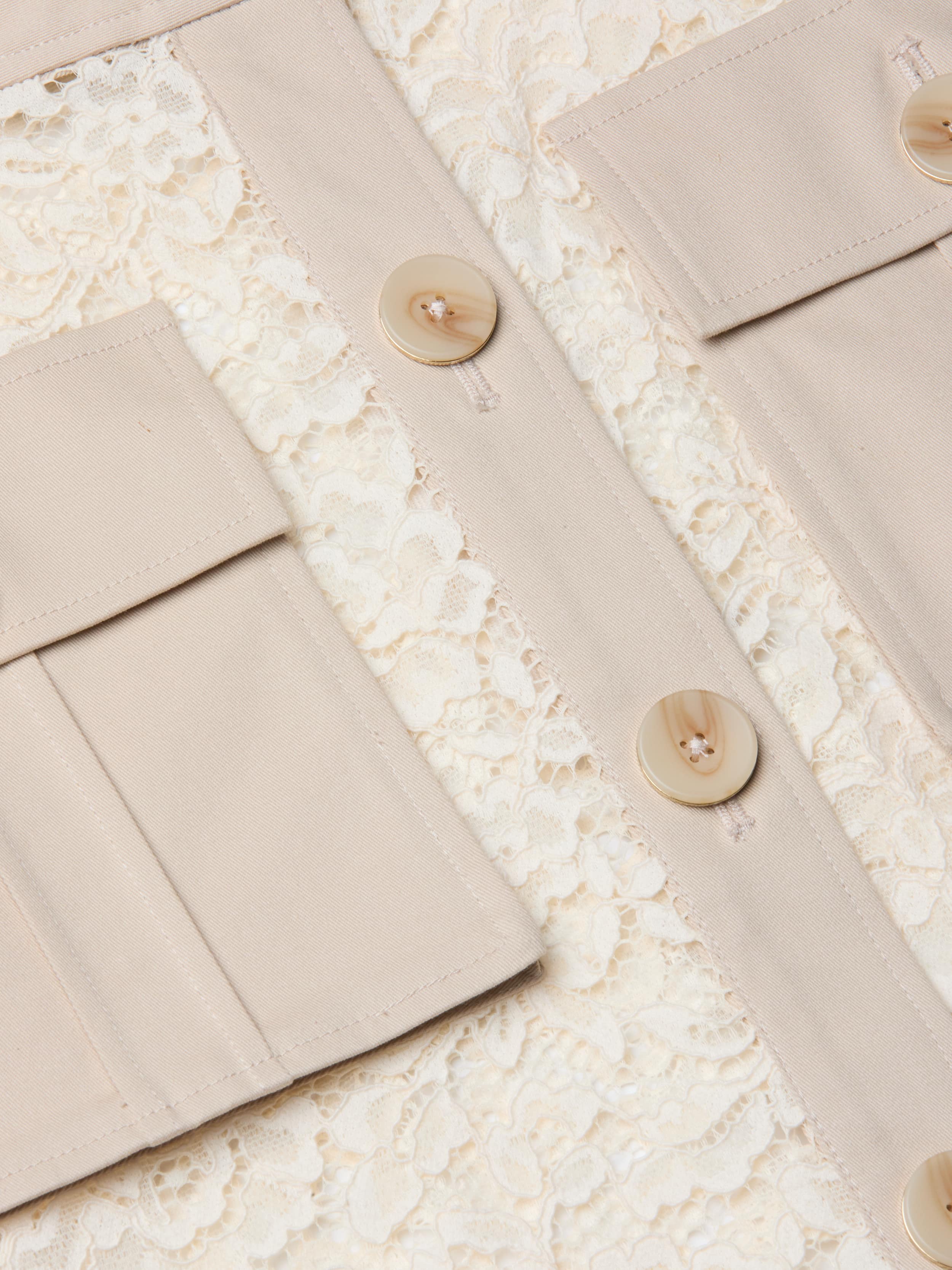 Close-up of the Shae Skirt featuring cream-colored floral lace fabric, beige panels, cargo pockets, and large beige buttons stitched vertically.