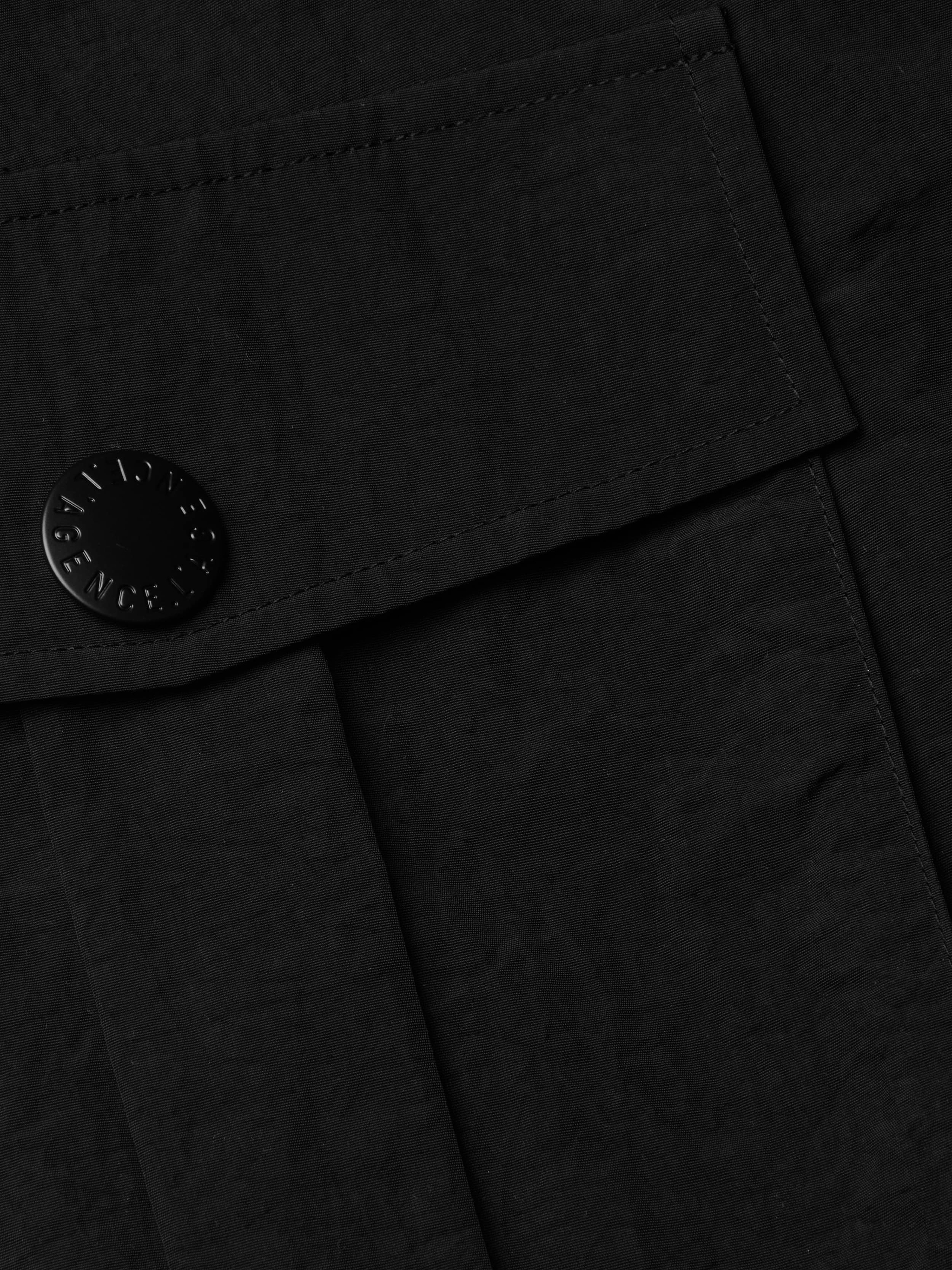 Close-up of the Norene Nylon Mini Skirt’s black fabric pocket with a flap, showcasing a round embossed button. The slightly crinkled, water-repellent nylon and neat stitching evoke classic cargo style.
