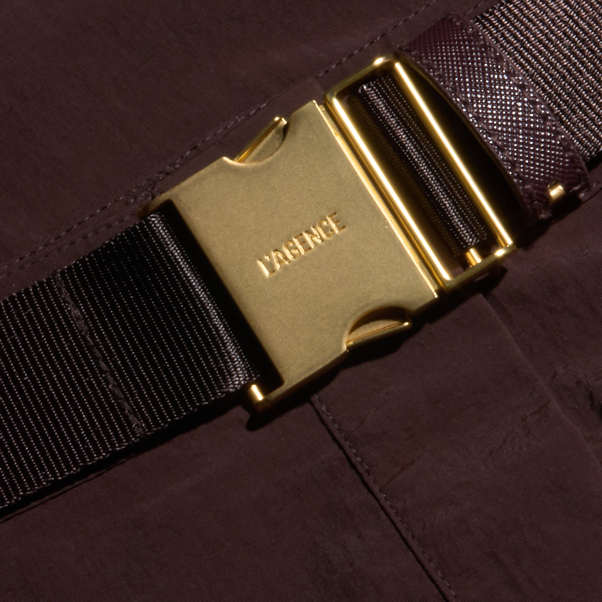 Close-up of a gold-colored metal buckle engraved with MAGNETIC on a dark brown fabric strap, attached to the Norene Nylon Mini Skirt in water-repellent brown textile.