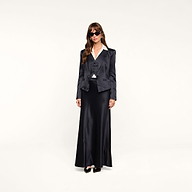 A woman wearing sunglasses, a dark blazer, and the Vespera Suspender Maxi Skirt stands against a plain white background.