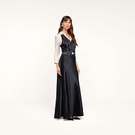 Wearing the Vespera Suspender Maxi Skirt, a woman poses against a plain white background, styling the long black pinstripe skirt with a fitted vest-style top over a white blouse.
