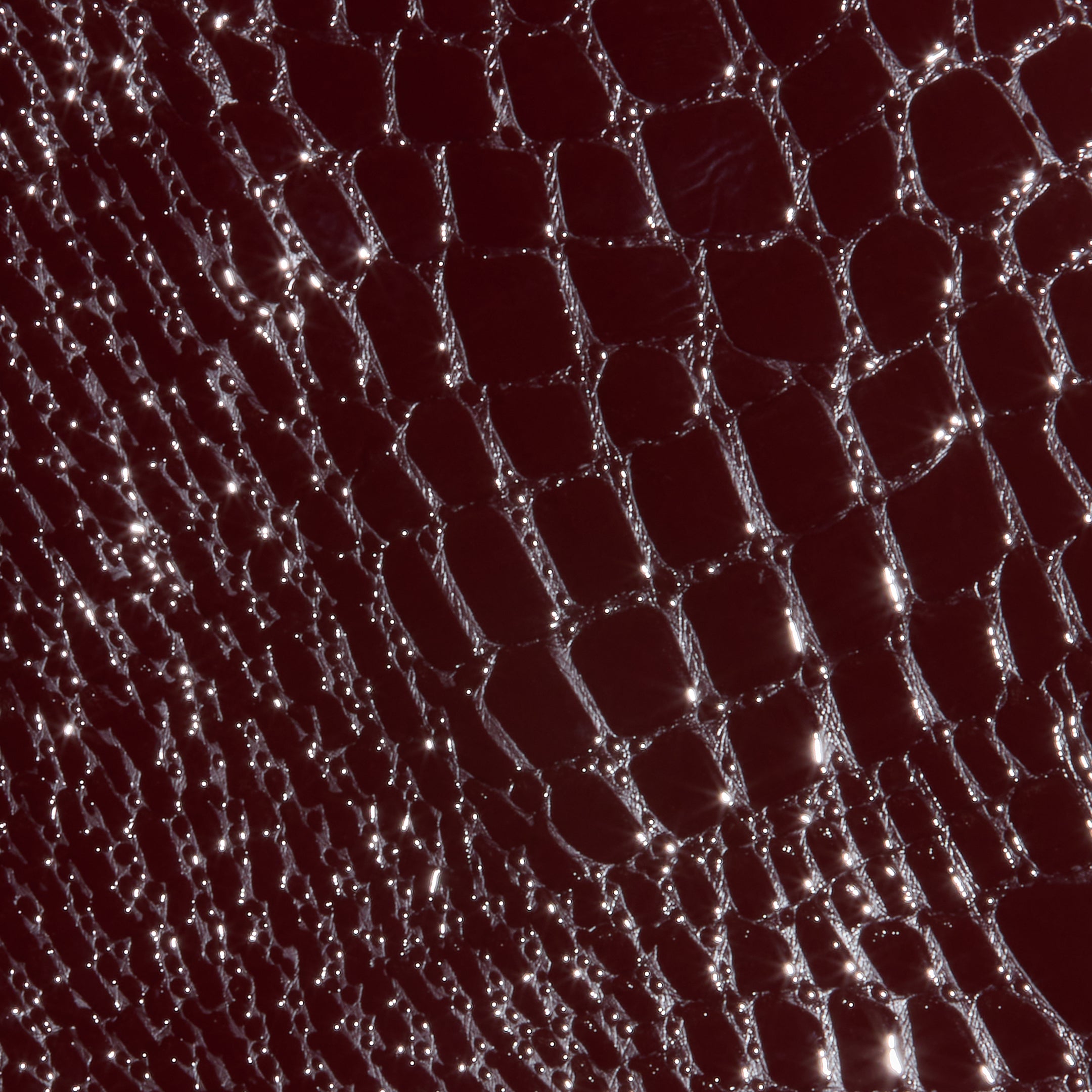 Close-up of the Violetta Vegan Leather Skirt, showcasing its shiny, burgundy croc-embossed texture with a pattern of irregular, reflective scales.