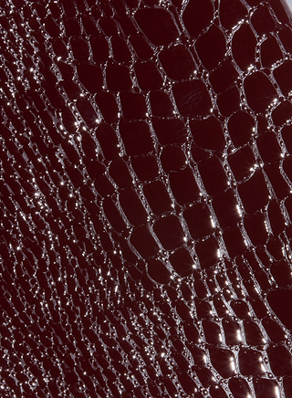 Close-up of a shiny, dark red, textured surface resembling croc-embossed vegan leather with a pattern of irregular, raised scales—perfect inspiration for the Violetta Vegan Leather Skirt in Fall 2026 fashion.