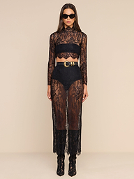 Woman wearing a black chantilly lace sheer long-sleeve crop top paired with the Raymonde Lace Maxi Skirt, standing against a beige background, accessorized with sunglasses and ankle boots—an effortlessly chic look perfect for a night out.